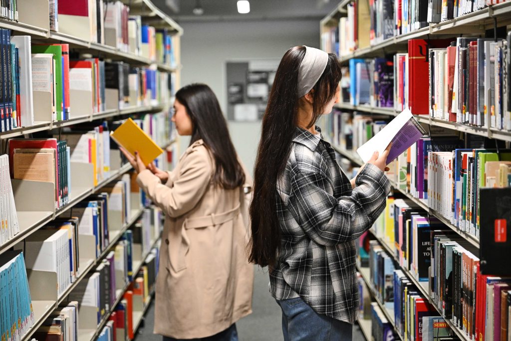 Two students reading booking next to bookcases in the library